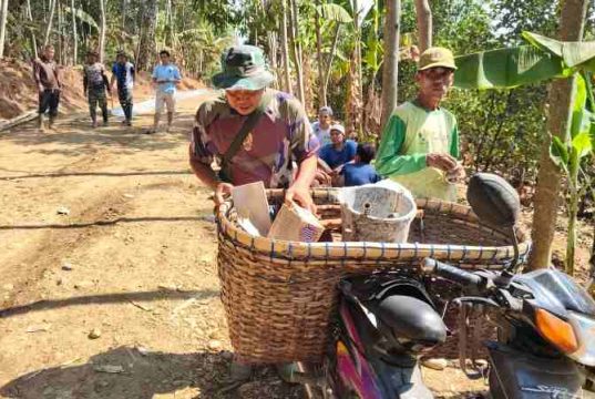 Semangat Anggota Satgas TMMD, Tetap Enjoi Mengendarai Sepeda Motor Sambil Membawa Keranjang Berisi Alat Tukang